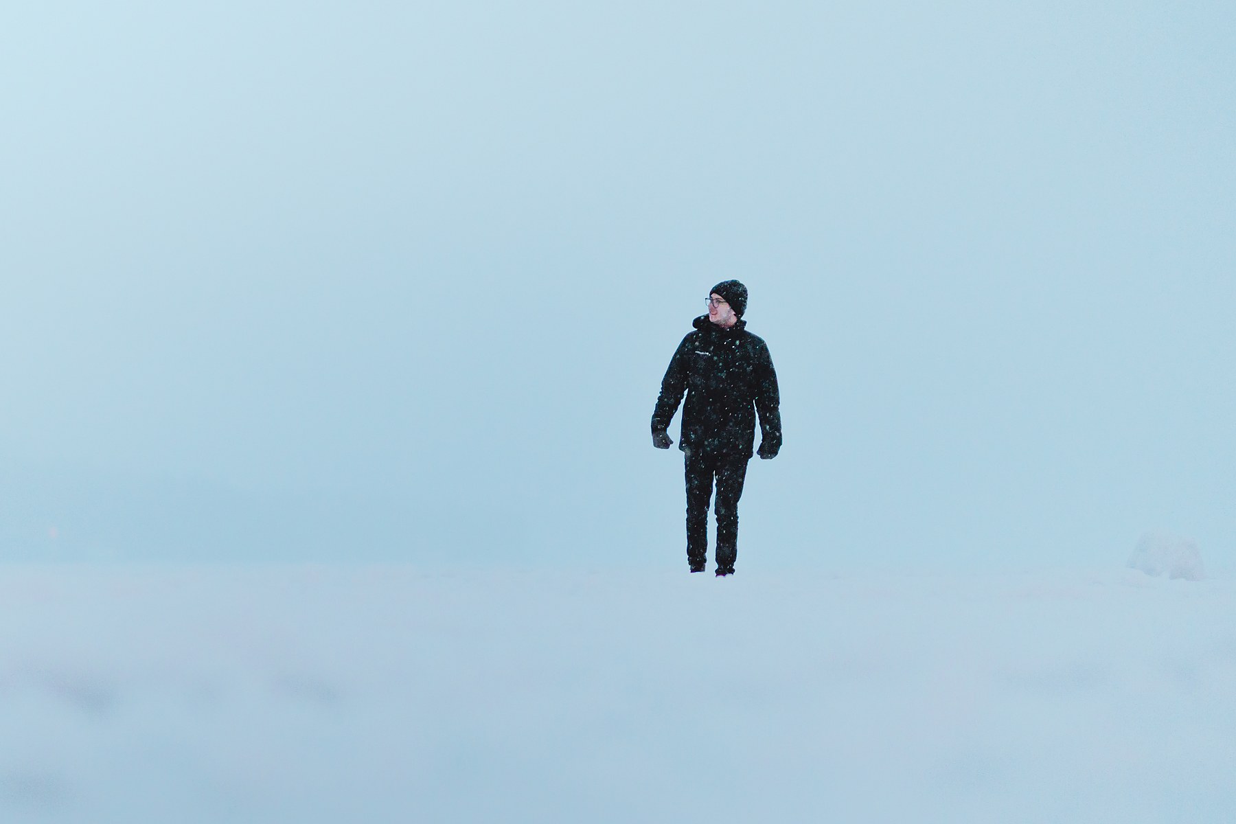 Walking alone across an empty snowfield under pale winter light