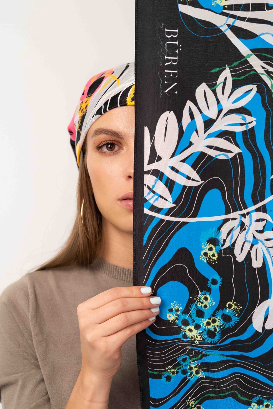A model on a white background, half her face covered by a black and blue printed pashmina